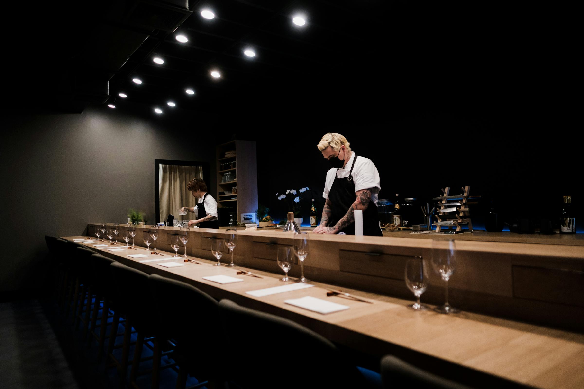 Chefs preparing sushi at the Kurosei counter in low light